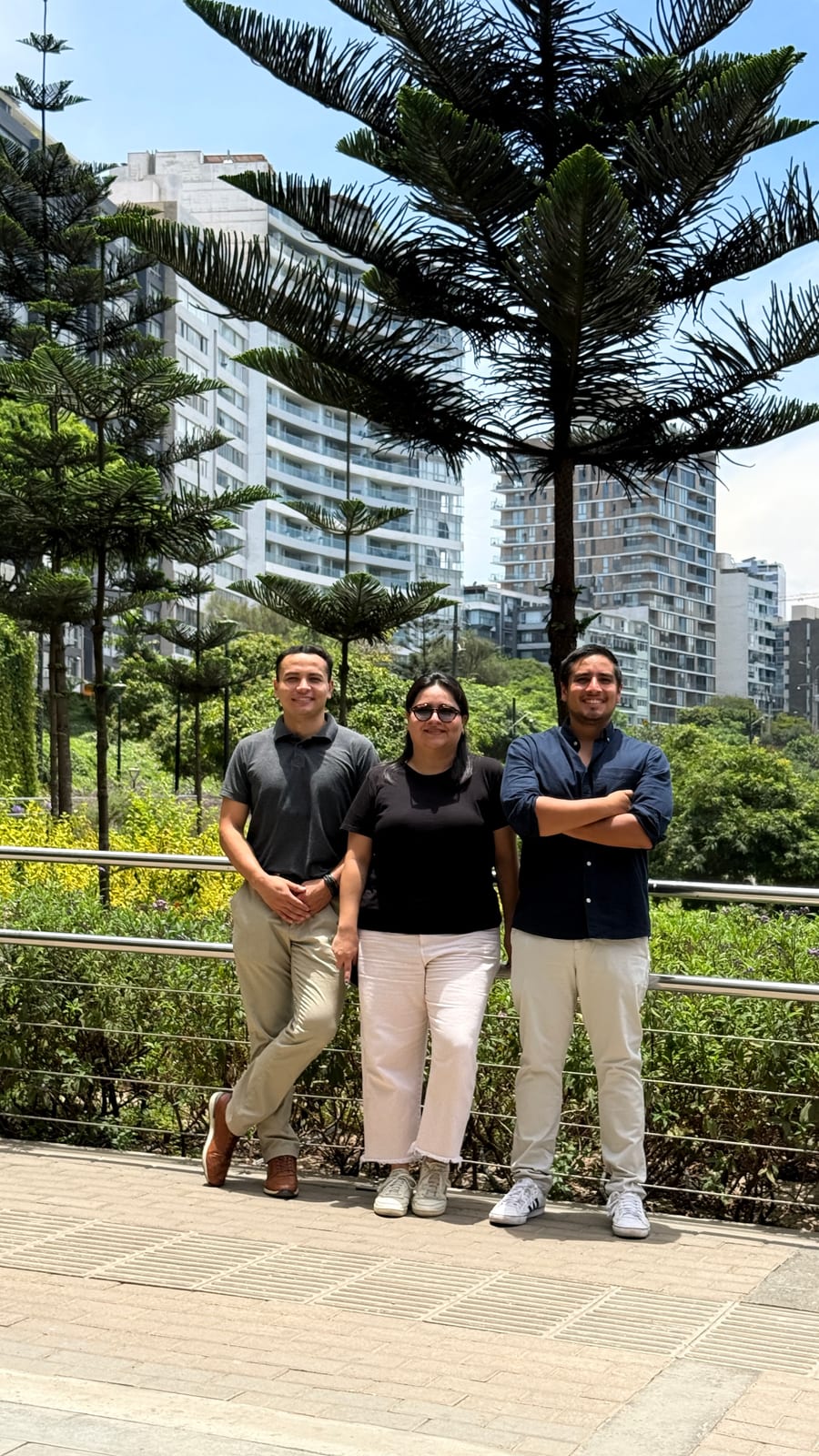 Tres integrantes del equipo de R'HOME en un parque, con una araucaria y edificios residenciales al fondo
