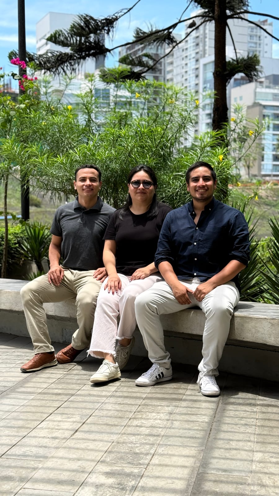 Tres integrantes del equipo de R'HOME sentados en una banca de concreto, con edificios al fondo
