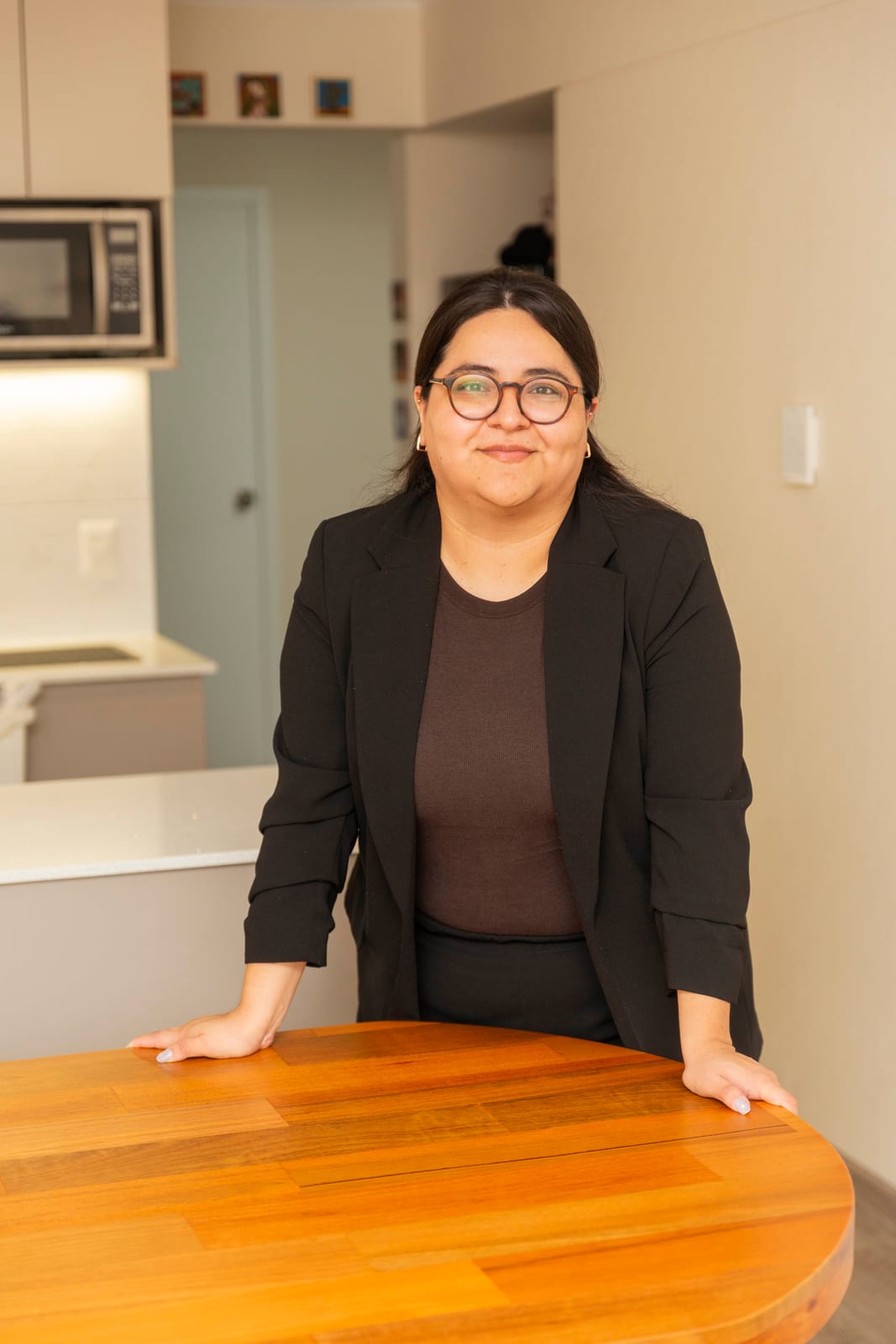 Integrante del equipo de R'HOME apoyada en la mesa del comedor, con la cocina del departamento al fondo